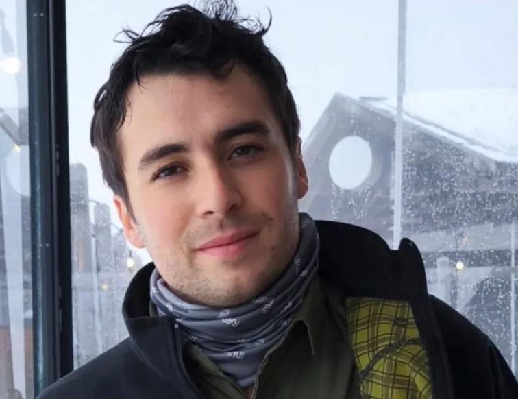 Facu sonriendo, con cuello polar y campera, frente a una ventana mojada por la lluvia.